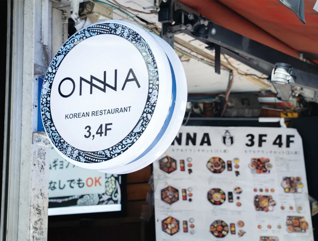 「ONNA」と書かれた丸い看板とその奥にメニュー表が掲示されています。