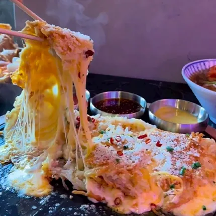 とろけるチーズが伸びる爆弾チーズチヂミを箸で持ち上げた、熱々で食欲をそそる一枚です