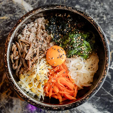 石焼きの器に彩り豊かな野菜と肉、中央に卵黄がのったビビンバが丁寧に盛り付けられています