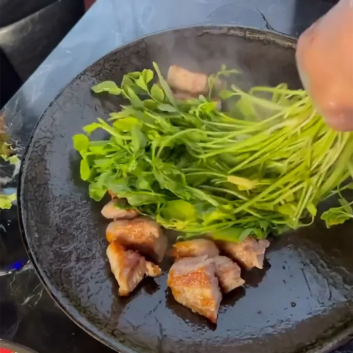 鉄板の上で焼いた豚肉に新鮮なミナリをのせて一緒に調理している