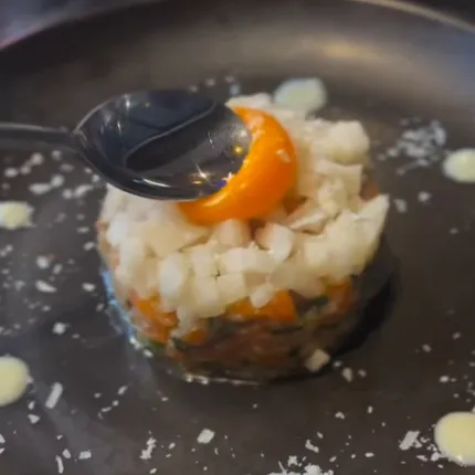 黒い皿の上にサーモンユッケが盛られ、刻み玉ねぎと卵黄が美しく添えられています