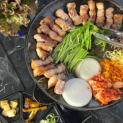 鉄板の上でサムギョプサルと野菜、キムチ、玉ねぎが彩りよく並び、食欲をそそる一枚です