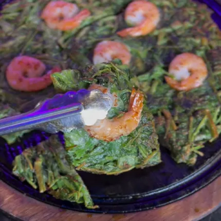 熱々の鉄板からエビ入りミナリチヂミを持ち上げた、香ばしさが伝わる一枚です