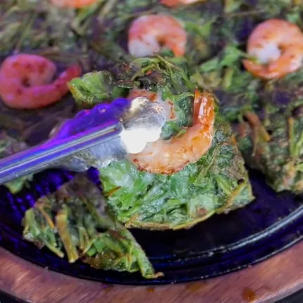 熱々の鉄板からエビ入りミナリチヂミの一片をトングで持ち上げた、香ばしさが伝わる一枚です