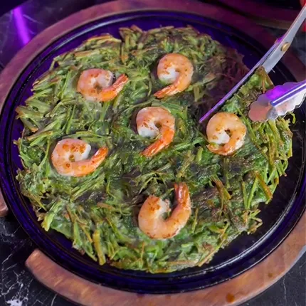 丸い鉄板の上でエビ入りミナリチヂミが香ばしく焼かれ、湯気が立つ食欲そそる一枚です