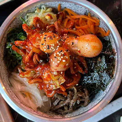 金属の器に辛いチュクミと野菜が彩りよく盛られ、香ばしい胡麻が散りばめられたビビンバです