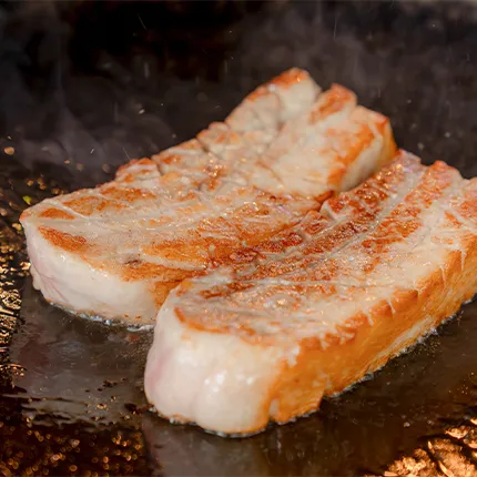 鉄板の上で厚切りの豚バラ肉が音を立てて焼かれている様子